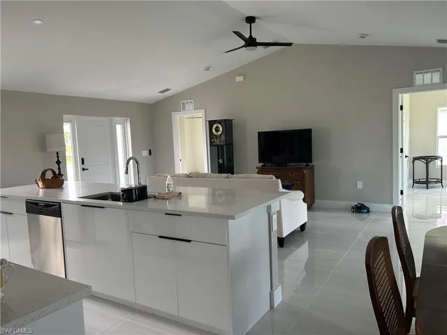 Modern kitchen island featuring a stainless steel dishwasher, an undermount sink with a gooseneck faucet, and white slab-front cabinetry with linear pulls