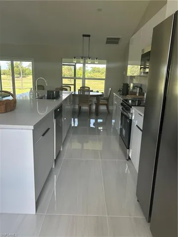 Modern kitchen featuring a large island with a stainless steel sink, sleek white cabinetry, and stainless steel appliances