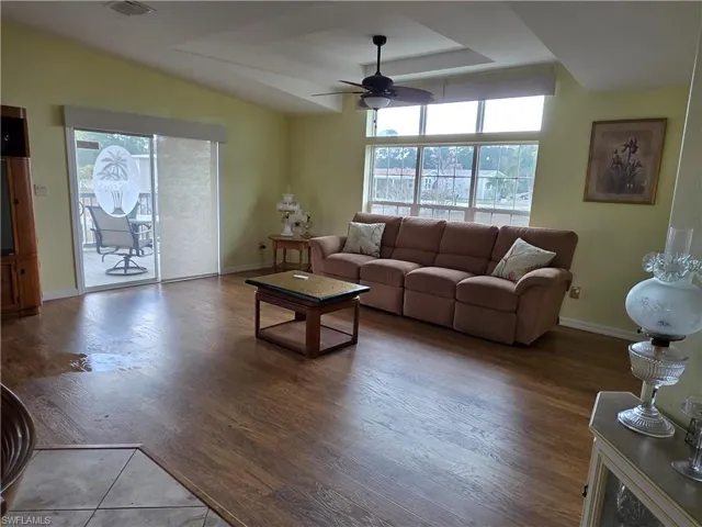 Living room with a ceiling fan, plenty of natural light, wood finished floors, and a tray ceiling