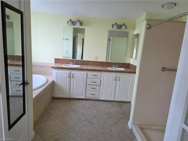 Bathroom featuring double vanity, light tile patterned floors, a garden tub, and a shower stall