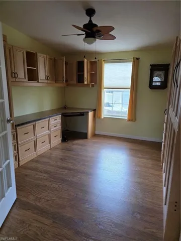 Kitchen with built in study area, open shelves, a ceiling fan, dark countertops, and dark wood-type flooring
