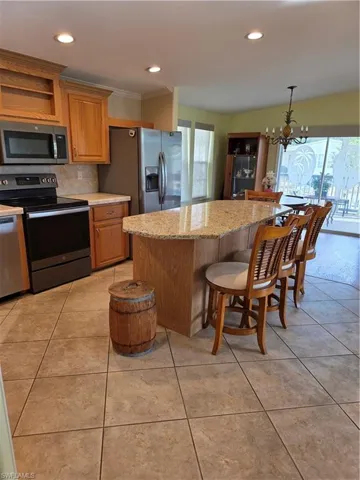Kitchen featuring stove, a kitchen breakfast bar, a kitchen island, refrigerator, and suspended lighting