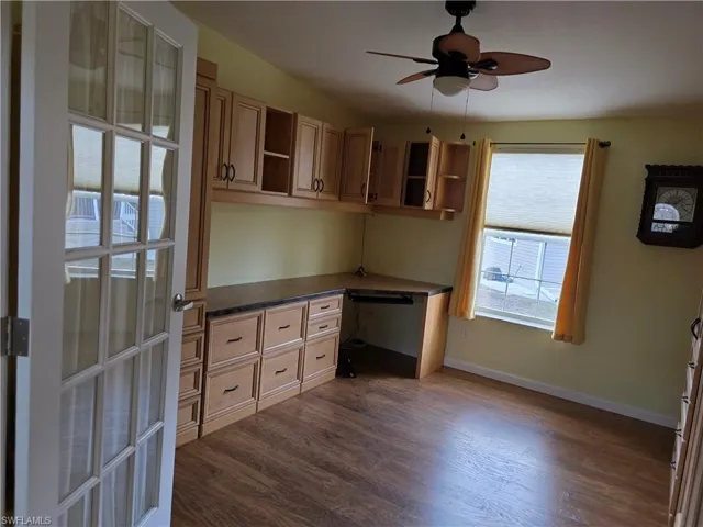 Unfurnished office with built in study area, ceiling fan, and dark wood-style flooring