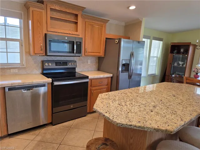 Kitchen featuring stainless steel appliances, a breakfast bar area, tasteful backsplash, light tile patterned floors, and a kitchen island