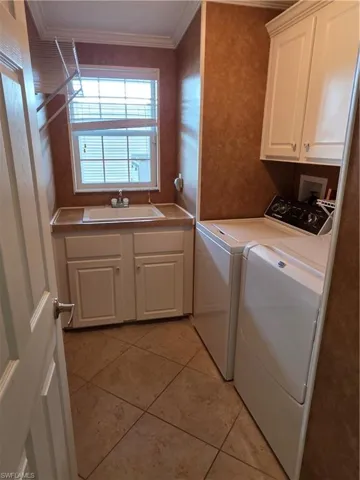 Laundry area featuring cabinet space, separate washer and dryer, crown molding, and light tile patterned flooring
