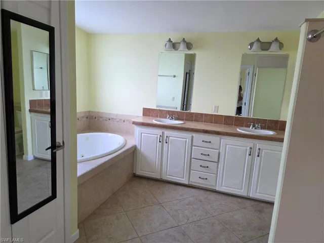 Full bathroom with double vanity, a garden tub, and light tile patterned floors