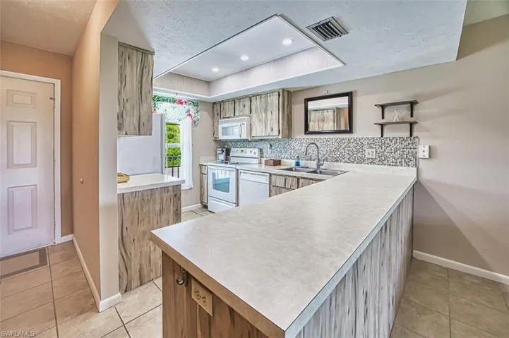 Kitchen with a textured ceiling, white appliances, light tile patterned floors, light countertops, and open shelves