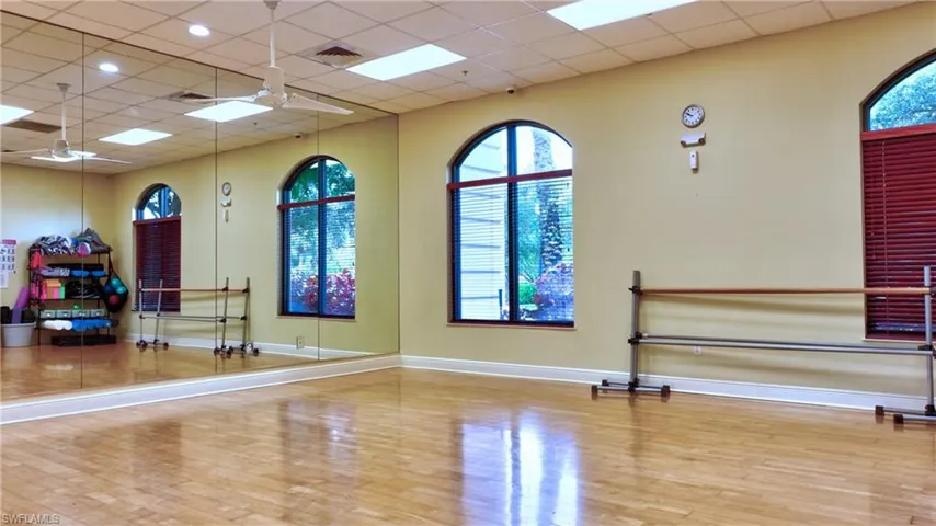 Exercise area with wood finished floors, baseboards, ceiling fan, and a drop ceiling