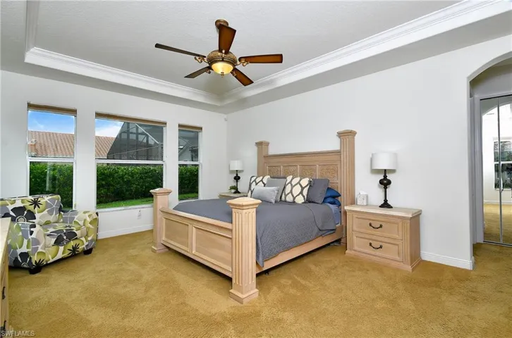 Bedroom featuring light colored carpet, a tray ceiling, crown molding, arched walkways, and baseboards