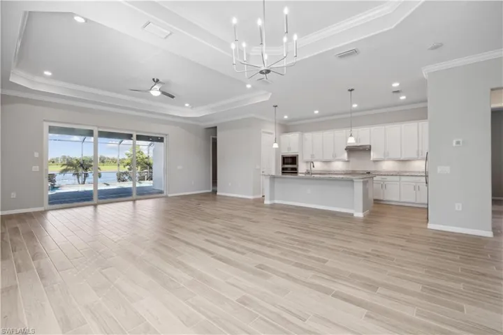 Great room featuring ceiling fan with notable chandelier, crown molding, and a raised ceiling