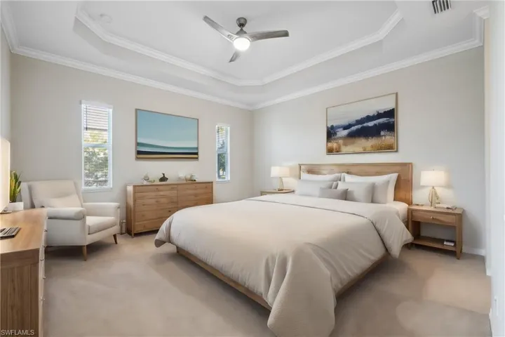Carpeted bedroom with ornamental molding, ceiling fan, and a tray ceiling
