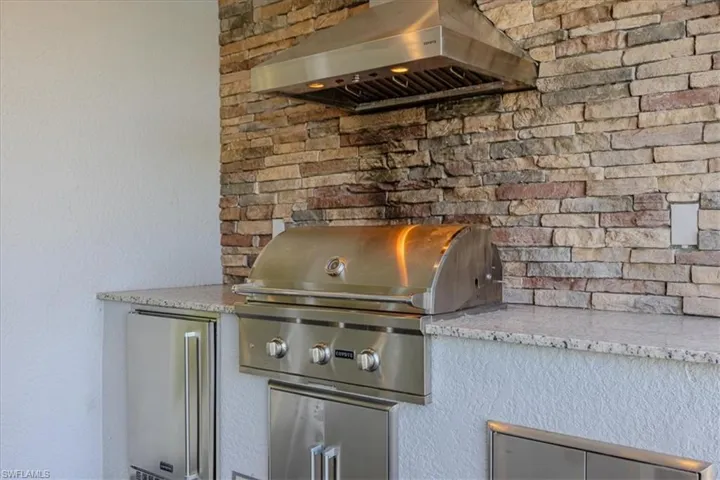 Summer kitchen with light stone countertops, wall chimney exhaust hood, and refrigerator