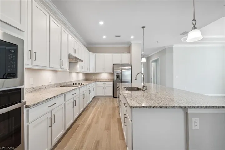 Kitchen with black appliances, white cabinets, light wood-type flooring, ornamental molding, and sink