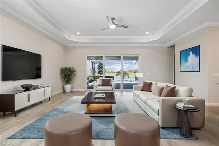 Great room with crown molding, light wood-type flooring, ceiling fan, and a raised ceiling