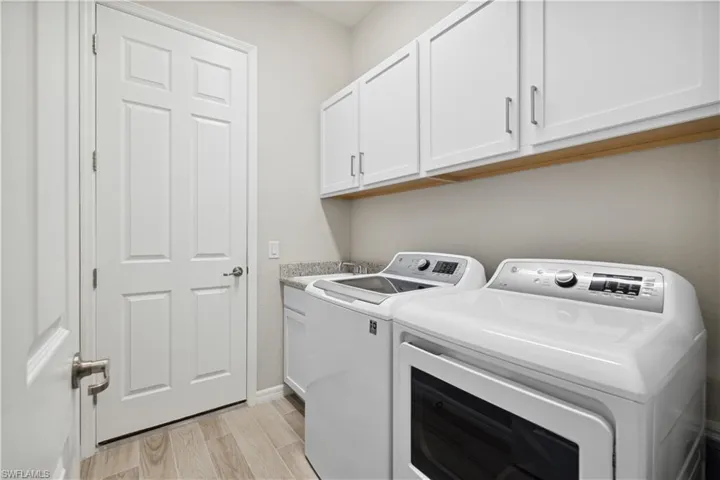 Laundry area featuring washing machine and clothes dryer, light hardwood / wood-style  tile floors, sink, and cabinets