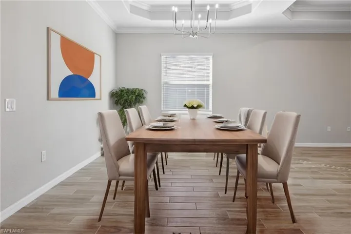 Dining area with an inviting chandelier, crown molding, light wood-look tile  flooring, and a tray ceiling