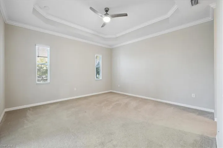 Spacious Master Bedroom featuring ceiling fan, carpet, a tray ceiling, and ornamental molding