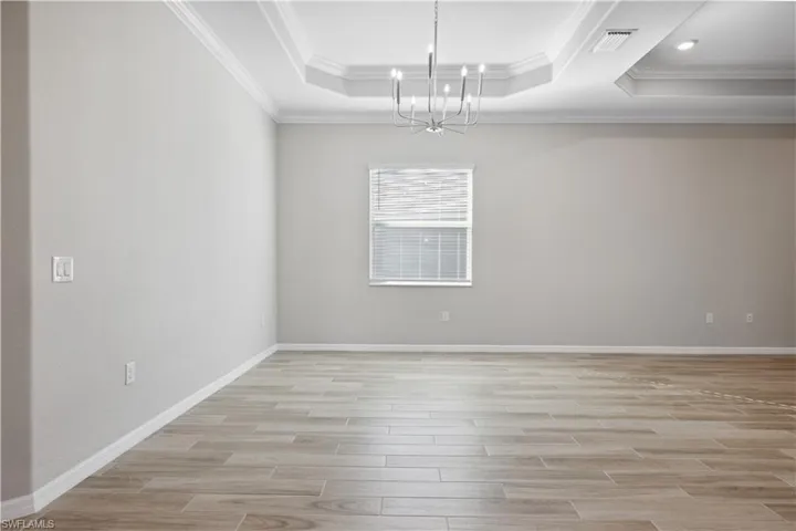 Dining area with light tile / wood-style flooring, an inviting chandelier, crown molding, and a raised ceiling