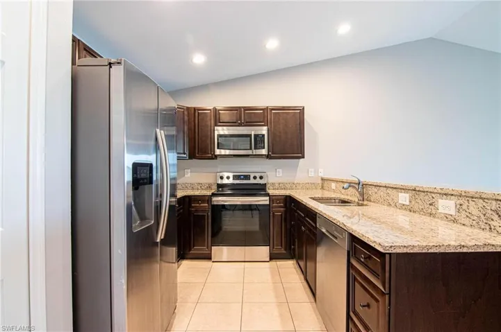 Kitchen with dark wood finish cabinetry, stainless steel appliances, light stone counters, light tile patterned flooring, and a peninsula