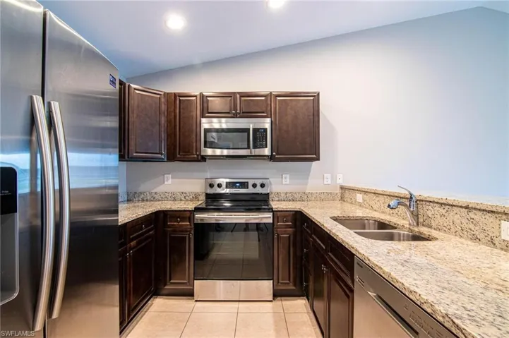 Kitchen with stainless steel appliances, light stone countertops, dark wood finish cabinets, vaulted ceiling, and light tile patterned floors