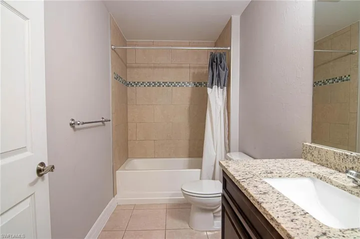 Full bath with vanity, shower / tub combo, light tile patterned floors, and a textured wall