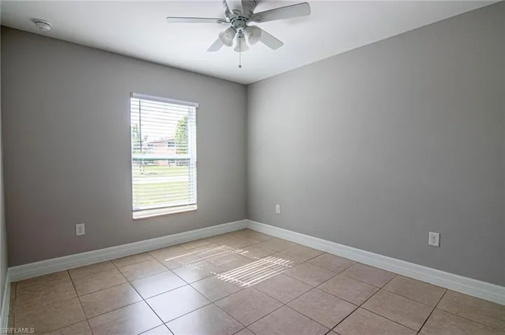 Empty room with ceiling fan, light tile patterned floors, and a smoke detector