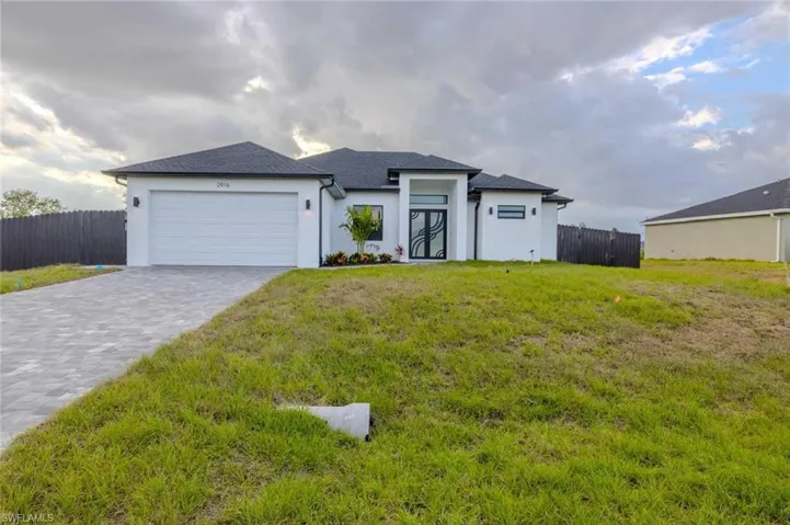 Prairie-style house with fence, an attached garage, stucco siding, a front yard, and decorative driveway