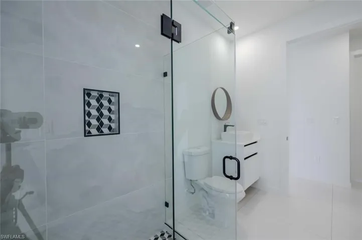 Bathroom with toilet, tile patterned floors, tiled shower, and vanity