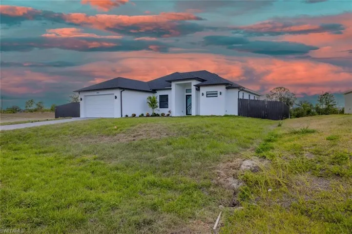 Prairie-style house with fence, an attached garage, a front lawn, stucco siding, and driveway