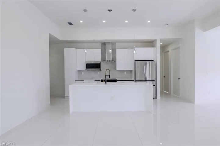 Kitchen with wall chimney range hood, a sink, stainless steel appliances, white cabinetry, and modern cabinets