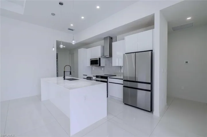 Kitchen with wall chimney range hood, visible vents, appliances with stainless steel finishes, a sink, and white cabinetry