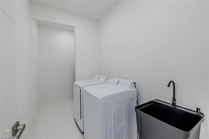 Clothes washing area featuring laundry area, a sink, light tile patterned floors, and washing machine and dryer