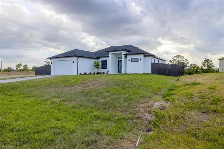 Prairie-style home with fence, a garage, stucco siding, a front yard, and driveway