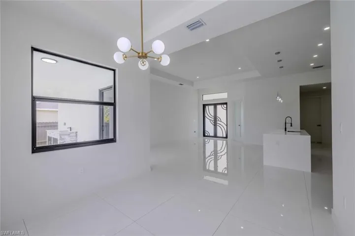 Tiled empty room with visible vents, a sink, a raised ceiling, and a notable chandelier