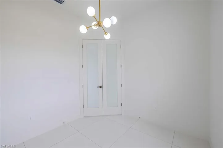 Empty room with light tile patterned floors and a notable chandelier