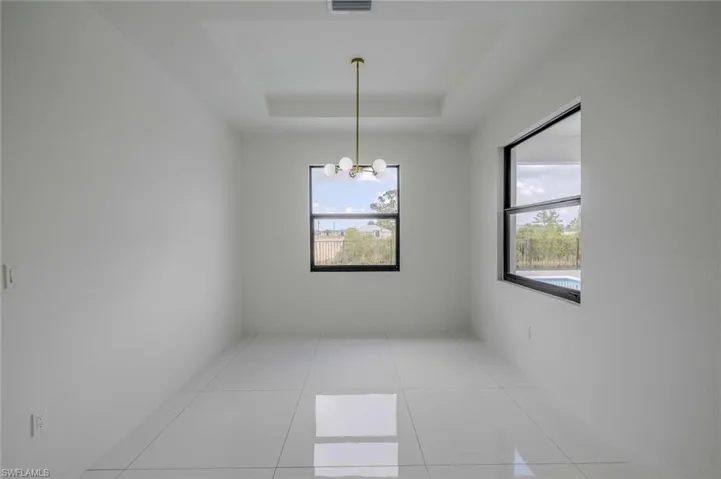 Spare room with light tile patterned floors, a raised ceiling, visible vents, and a chandelier