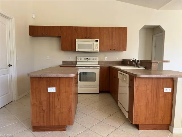 Kitchen with a peninsula, light tile patterned flooring, a sink, and white appliances