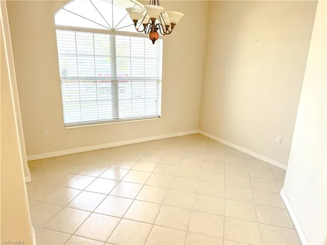 Empty room featuring light tile patterned floors, baseboards, and an inviting chandelier
