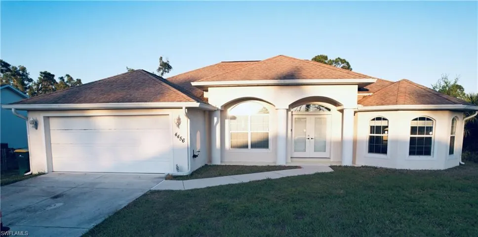 View of front of home with stucco siding, a front yard, french doors, a garage, and driveway