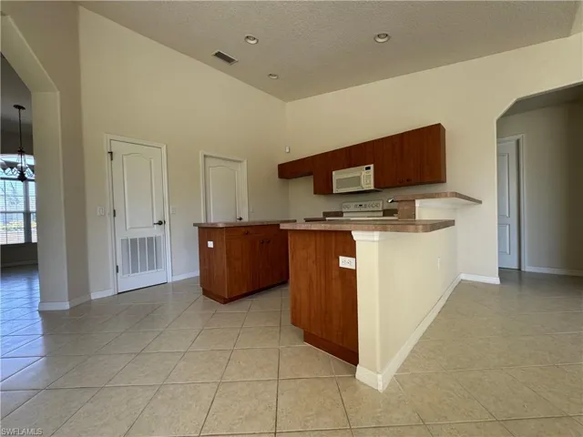 Kitchen featuring a textured ceiling, light tile patterned flooring, white appliances, an inviting chandelier, and a peninsula