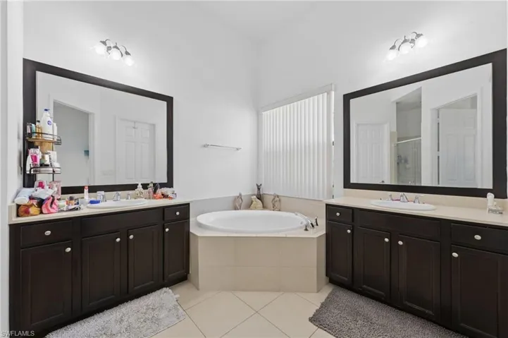 Full bath featuring two vanities, a shower stall, light tile patterned floors, and a garden tub