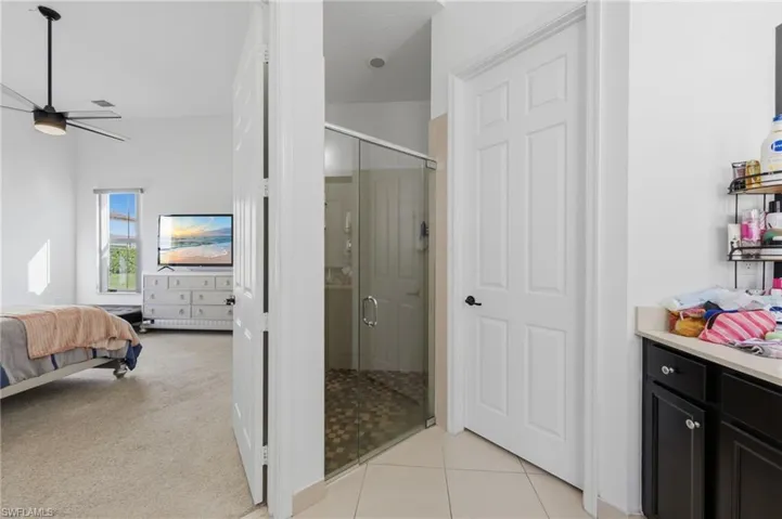 Full bathroom with connected bathroom, a shower stall, light carpet, a ceiling fan, and light tile patterned floors