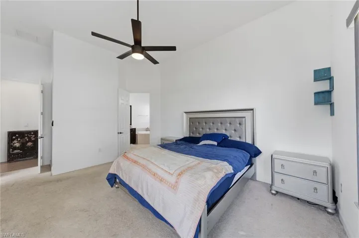 Bedroom featuring light carpet, a ceiling fan, ensuite bathroom, and lofted ceiling
