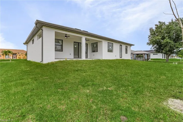 Rear view of property featuring a lawn, ceiling fan, and a gazebo