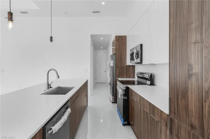 Kitchen with appliances with stainless steel finishes, hanging light fixtures, sink, and white cabinets