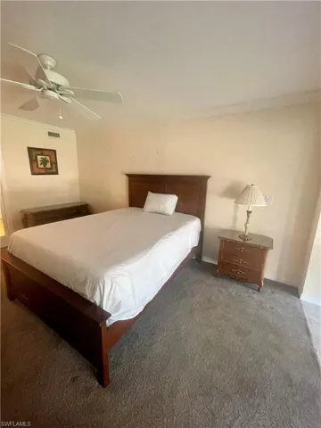 Bedroom with ceiling fan, dark colored carpet, and crown molding