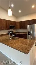 Kitchen featuring stainless steel appliances, hanging light fixtures, dark wood finish cabinetry, and dark stone counters