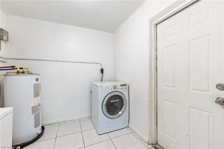 Laundry area with washer / clothes dryer, light tile patterned floors, and water heater