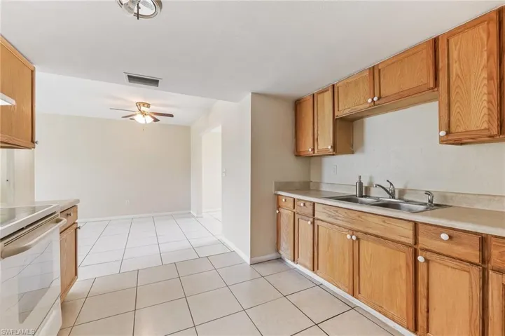 Kitchen with white electric range oven, light tile patterned flooring, light countertops, ceiling fan, and brown cabinetry