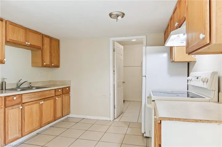 Kitchen featuring white electric stove, light countertops, under cabinet range hood, and light tile patterned flooring